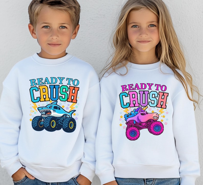 boy and girl are wearing matching white sweatshirts. The boy's says "ready to Crush" in Varsity Style multiple colors in an arch . underneath is a blue shark monster truck megalodon cartoon style. The girl's says Ready to Crush in Pink Varsity Letters - Multi-colored with a Pink Unicorn Monster Truck Sparkle Crash Smash cartoon style. Perfect to wear for car shows and truck racing events. Monster Truck Jam, Birthday Gifts and Pit Crew Parties. Parent and Sibling , grandparent, Family Matching
