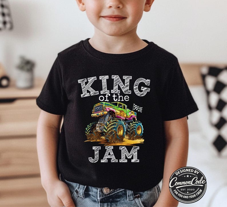 May include: Black t-shirt featuring a colourful monster truck graphic and the text "KING of the JAM". The monster truck is green, pink, and blue. The shirt also has the text "DESIGNED BY Common Code EST. 2020 FOR YOU AND YOUR CREW".