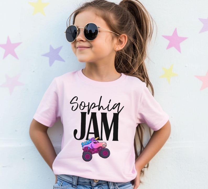 Girl is wearing a pink Monster Truck Jam t-shirt that has a unicorn Monster Truck Jam Themed t-shirt that says "Sophia" Jam with a unicorn Monster Truck in Rainbow Colors of Pink, Purple and Blue in a cartoon style drawing. The name is fully customizable in a cursive style font, JAM is in a bold block print. The letters are in black. Comes Family Matching sizes perfect for birthday Girl Parties, Race Day, Truck Show apparel.