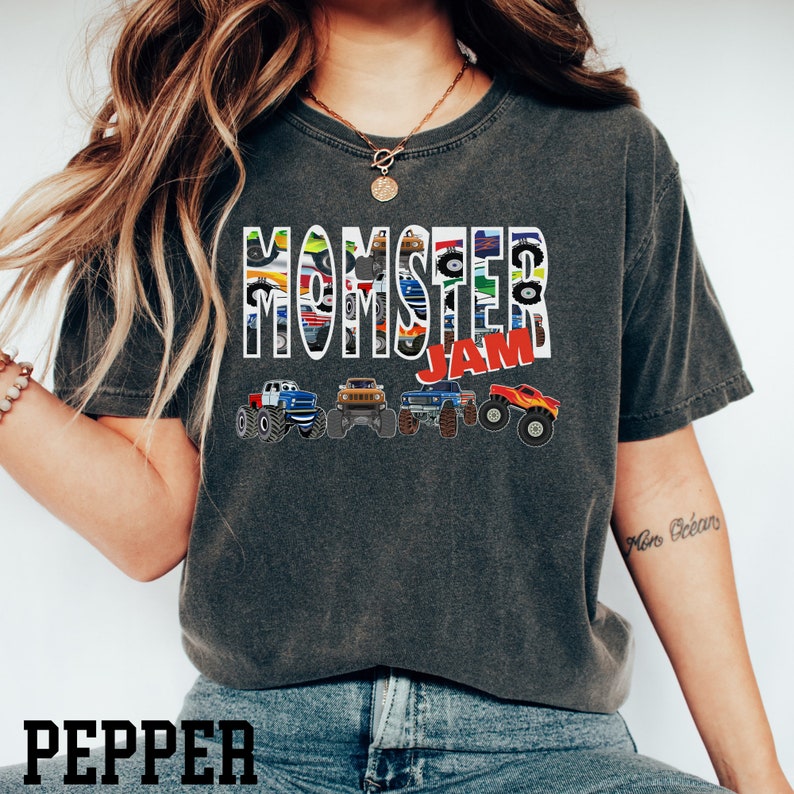 May include: A dark grey t-shirt with the words "MOMSTER JAM" printed on the front. The words are made up of images of monster trucks.