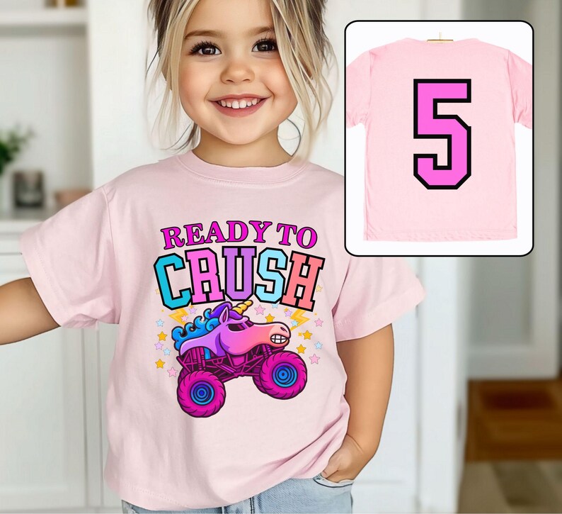 Pode incluir: T-shirt rosa claro com a frase "READY TO CRUSH" e um desenho de monster truck com cabe&ccedil;a de unic&oacute;rnio. A parte de tr&aacute;s da camiseta mostra o n&uacute;mero 5.
