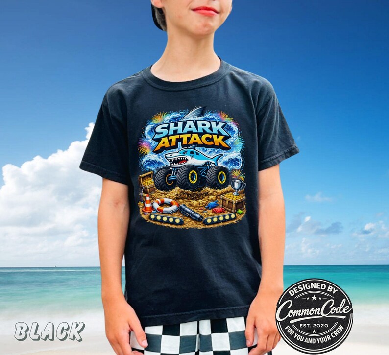 Puede incluir: Camiseta negra con un gr&aacute;fico colorido de "SHARK ATTACK" que muestra un cami&oacute;n monstruo tibur&oacute;n. El dise&ntilde;o incluye cofres del tesoro, un salvavidas y el texto "DESIGNED BY COMMON CODE FOR YOU AND YOUR CREW EST. 2020".