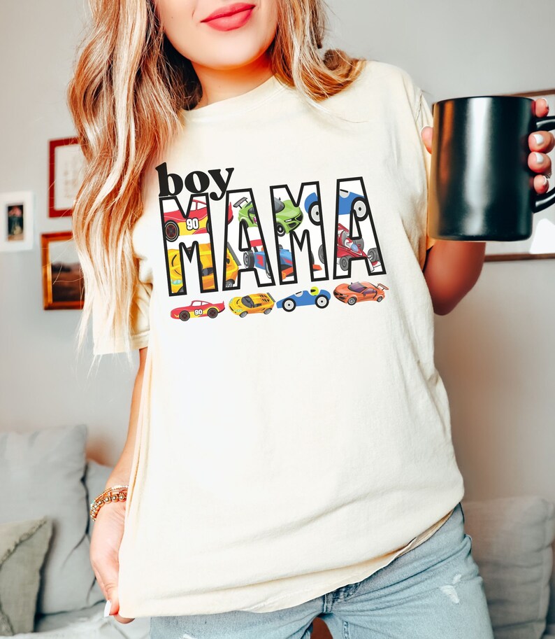 May include: A white t-shirt with the text "boy mama" in black letters. The letters are filled with colorful toy cars.