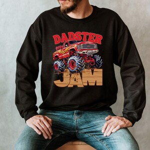 May include: Black sweatshirt featuring a graphic of a red monster truck with blue and red wheels, and the text "DADSTER JAM" in red and brown. The design has a vintage, cartoonish style.