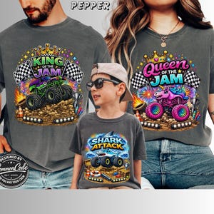 Peut inclure: Trois t-shirts gris avec des motifs de monster trucks color&eacute;s. L'un dit "King of the Jam", un autre "Queen of the Jam", et le troisi&egrave;me "Shark Attack". Les chemises sont port&eacute;es par une famille.