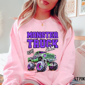 May include: Pink sweatshirt with a purple and green monster truck graphic and the text "Monster Truck Jam".