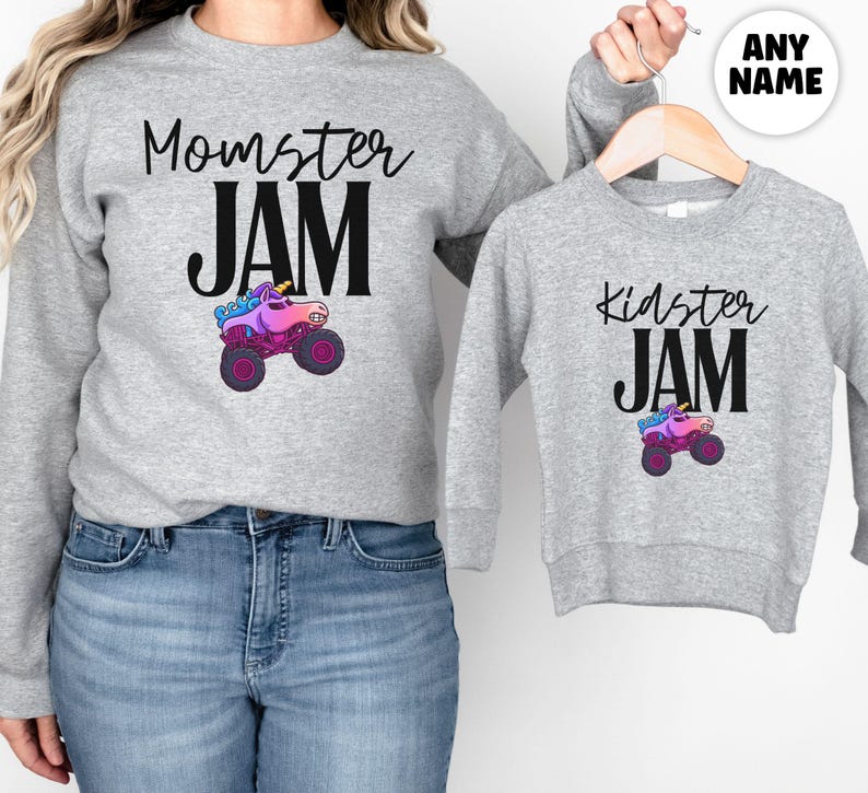May include: Two gray sweatshirts, one adult and one child size, with matching designs. The adult sweatshirt says "Momster JAM" with a monster truck graphic. The child's sweatshirt says "Kidster JAM" with a similar graphic. The monster truck is pink, purple, and blue.