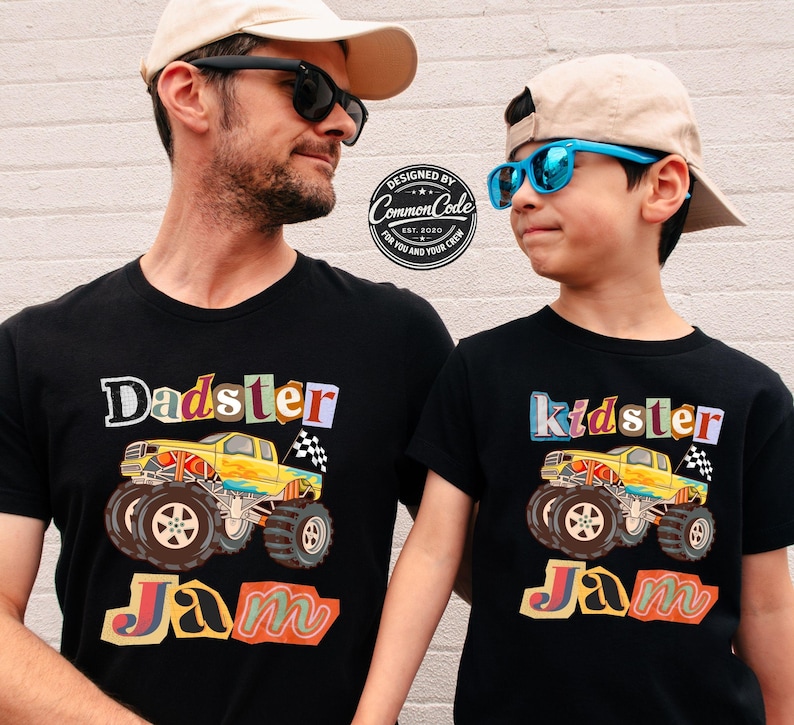 Puede incluir: Dos camisetas negras con gr&aacute;ficos coloridos. Una camiseta dice "Dadster Jam" con un dise&ntilde;o de cami&oacute;n monstruo amarillo. La otra dice "Kidster Jam" con un cami&oacute;n similar. Ambas camisetas tienen una bandera a cuadros.
