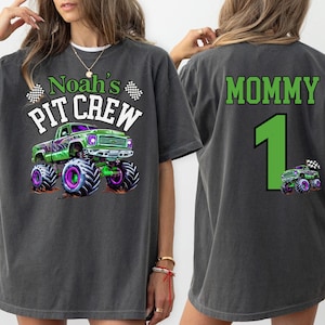 woman model is wearing a Monster Truck Jam  T-shirt in Pepper with a Green and Purple Monster Truck Digger themed graphic that says "Noah's Pit Crew" in Varsity Colligate Style Letters with 2 racing checkered flags.  The back print says "mommy" and the number 1 in green letters. perfect for monster truck celebration events. Family Matching for kids and adults. Custom personalized name and number on back.