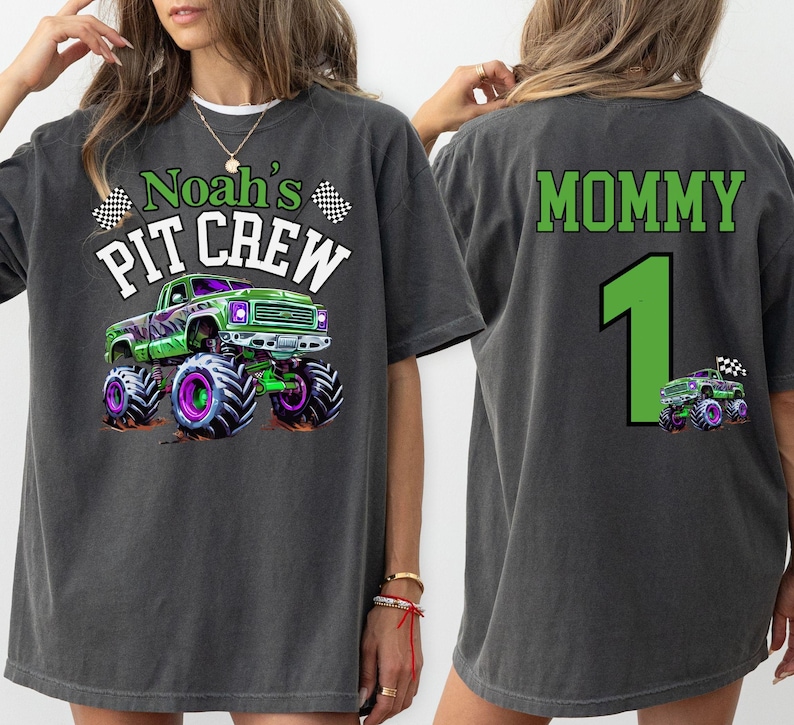 woman model is wearing a Monster Truck Jam  T-shirt in Pepper with a Green and Purple Monster Truck Digger themed graphic that says "Noah's Pit Crew" in Varsity Colligate Style Letters with 2 racing checkered flags.  The back print says "mommy" and the number 1 in green letters. perfect for monster truck celebration events. Family Matching for kids and adults. Custom personalized name and number on back.