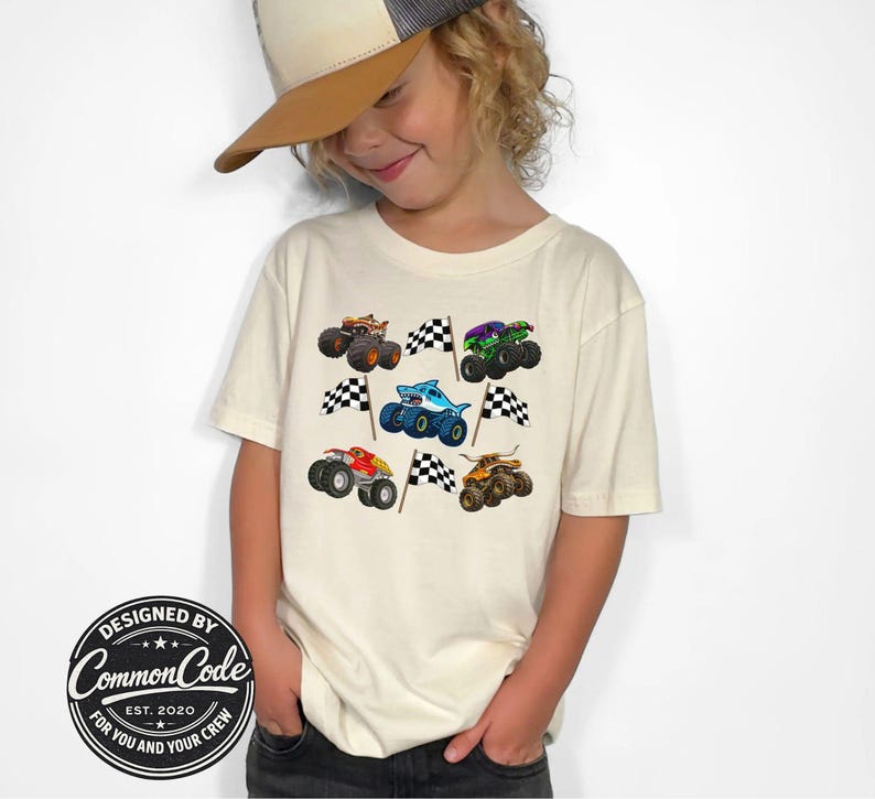 Boy in a natural cream colored t-shirt with various monster truck vehicles in cartoon style with racing checkered flags . Monster trucks jam themed with digger truck, shark megalodon truck, tiger shark truck, bull toro truck and dragon truck. Perfect for race day, monster truck birthday parties, kids gift, matching mommy daddy and mini shirts. Comes in Baby, toddler, kid, teen and adult sizes. Very colorful and vibrant fun graphic style shirt.