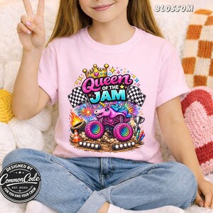 May include: A light pink t-shirt with a vibrant graphic of a unicorn monster truck and the words "Queen of the Jam". The design includes checkered flags, a crown, and a trophy. The shirt is designed by Common Code.