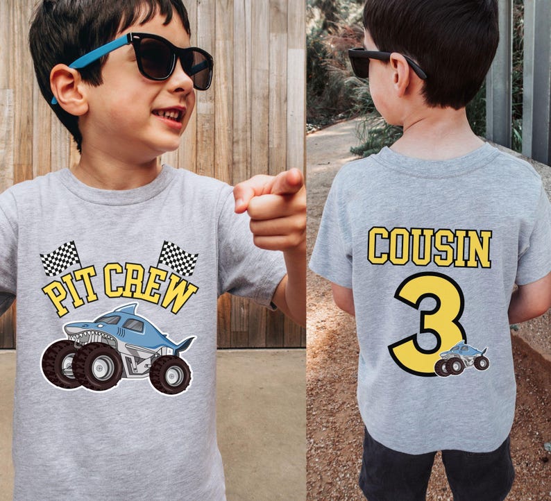 May include: A gray t-shirt with a shark monster truck graphic and the words "PIT CREW" in yellow. The back of the shirt says "COUSIN" and the number "3" in yellow. A small monster truck graphic is below the number.