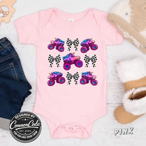 May include: A pink baby bodysuit with a repeating pattern of monster truck unicorns and checkered bows. The bodysuit has short sleeves and a round neckline. The text "DESIGNED BY Common Code" is printed on the bottom left.