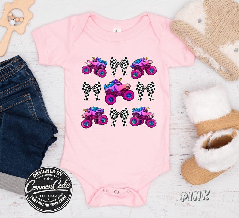 May include: A pink baby bodysuit with a repeating pattern of monster truck unicorns and checkered bows. The bodysuit has short sleeves and a round neckline. The text "DESIGNED BY Common Code" is printed on the bottom left.