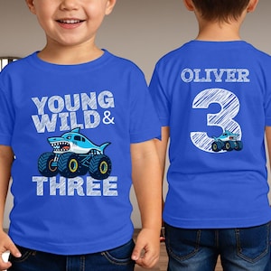 Op de afbeelding: Blauw T-shirt met een haaienmonster truck ontwerp. De voorkant zegt "Young Wild & Three". De achterkant toont de naam "Oliver" en het nummer "3" met een monstertruck.