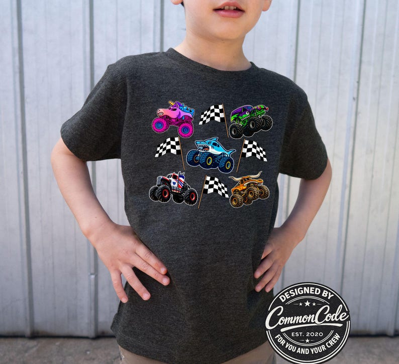 May include: A dark gray t-shirt featuring colorful monster truck graphics and checkered flags. The trucks have unique designs, including a shark, a unicorn, and a bull. The shirt has a round logo that says "Designed by Common Code Est. 2020 For You and Your Crew."