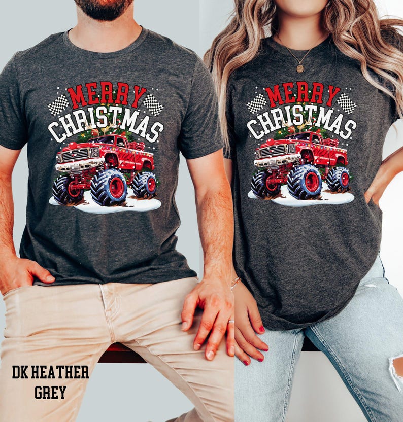 May include: Dark heather grey t-shirts with a red monster truck graphic and the text "MERRY CHRISTMAS". The truck has large tires and is set against a snowy background. The text "DK HEATHER GREY" is at the bottom.