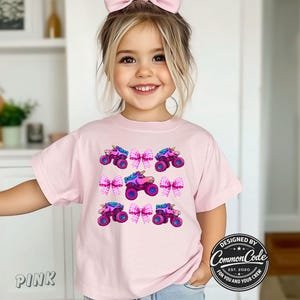 May include: A pink t-shirt with a repeating pattern of monster trucks with unicorn horns and pink bows. The shirt has the text "Pink" on the bottom left. The design is by Common Code.