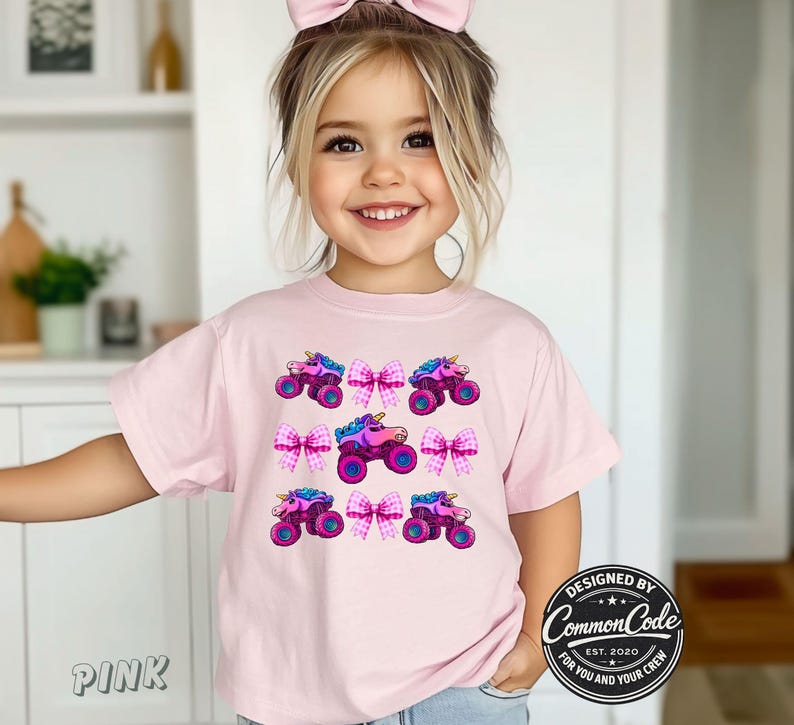 May include: A pink t-shirt with a repeating pattern of monster trucks with unicorn horns and pink bows. The shirt has the text "Pink" on the bottom left. The design is by Common Code.