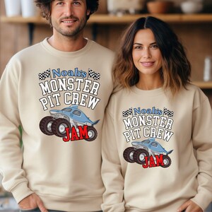 May include: Beige sweatshirts with the text "Noah's Monster Pit Crew" and a shark-themed monster truck graphic. The word "JAM" is in red. The sweatshirts are worn by two people.