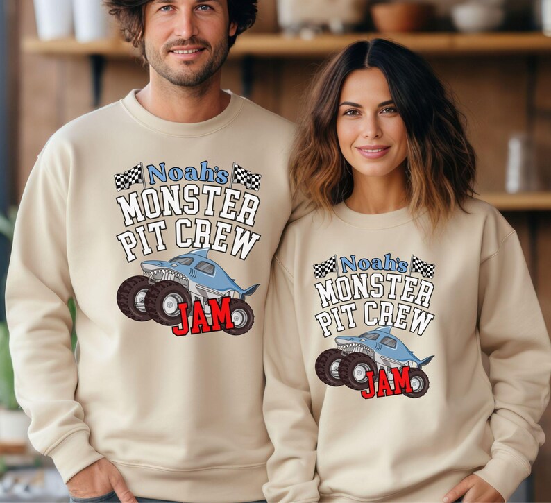 May include: Beige sweatshirts with the text "Noah's Monster Pit Crew" and a shark-themed monster truck graphic. The word "JAM" is in red. The sweatshirts are worn by two people.