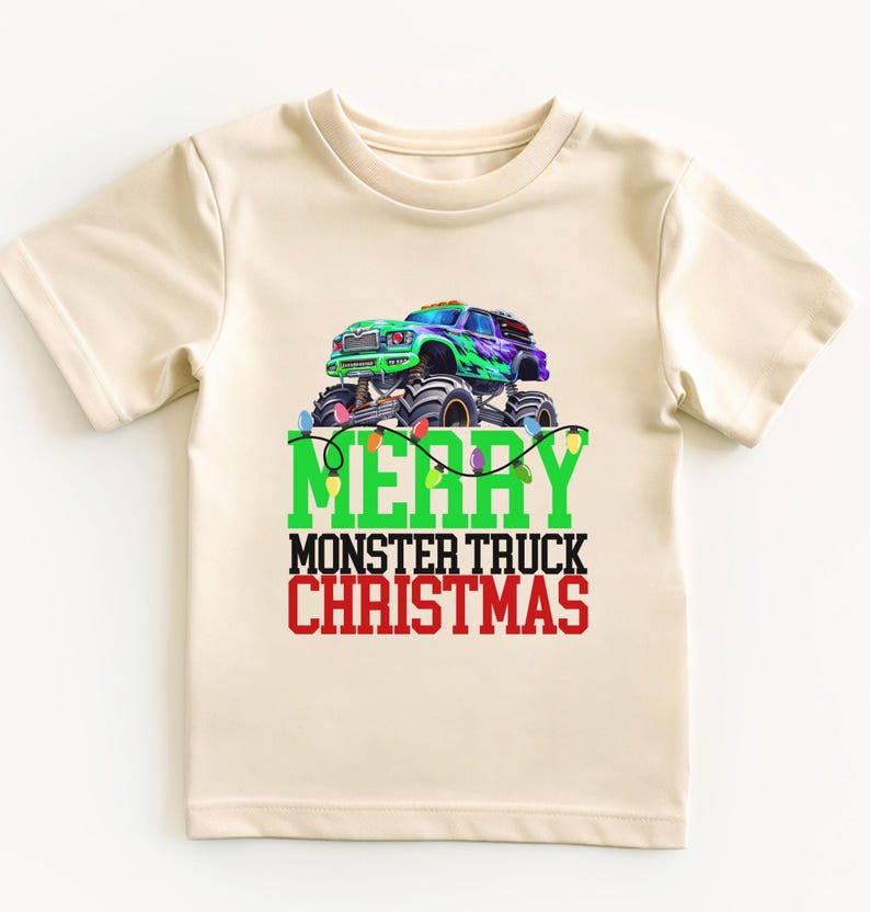 Puede incluir: Una camiseta beige de manga corta con un gr&aacute;fico de cami&oacute;n monstruo verde y el texto "Merry Monster Truck Christmas" en verde y rojo.
