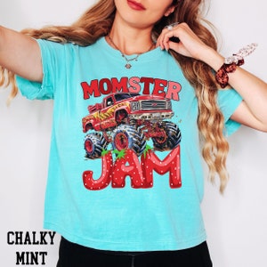 May include: A turquoise blue t-shirt with a red monster truck graphic and the text "Momster Jam" in red and white letters. The letters are made of strawberries.