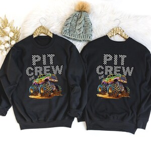 May include: Two black sweatshirts with a monster truck graphic and the text "PIT CREW" in white with black checkered flag accents.