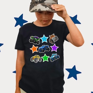 Może przedstawiać: Czarny t-shirt z kolorowymi grafikami monster truck&oacute;w otoczonymi gwiazdami. Ciężar&oacute;wki są w r&oacute;żnych kolorach, w tym zielonym, niebieskim, pomarańczowym i ż&oacute;łtym. Koszulka ma okrągły dekolt.