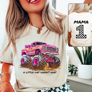 Woman Model is wearing a beige natural t-shirt showing the front and back side. The front has a Barbie Pink Monster Truck with black and white checkers. Underneath is a dirt floor with dirt and mud flinging up on the truck. It says "a little dirt doesn't hurt". The back says "Mama" and has a checkered number 1. Custom Name and number Monster Truck Jam Birthday Party Race Day Gift for Mom.