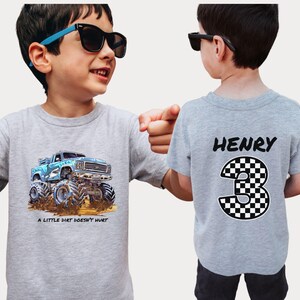 Peut inclure: Deux t-shirts gris. L'un pr&eacute;sente un dessin de camion monstre bleu avec le texte "A LITTLE DIRT DOESN'T HURT." L'autre t-shirt porte le nom "HENRY" et le chiffre "3" &agrave; damier au dos. Les deux t-shirts sont port&eacute;s par un enfant.