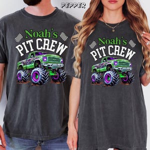 Pode incluir: Duas camisetas cinza escuro com o texto "Noah's PIT CREW" e um gr&aacute;fico de um caminh&atilde;o monstro verde com detalhes roxos e verdes. As camisetas s&atilde;o de manga curta e t&ecirc;m um corte folgado.