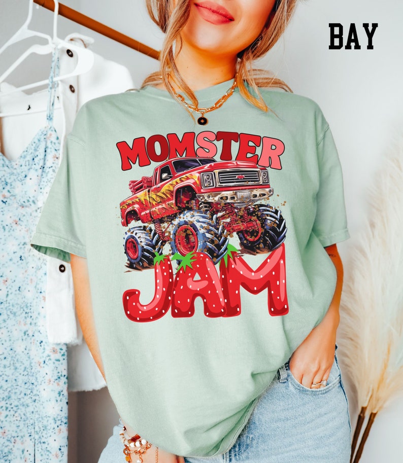 May include: A light green t-shirt with a red monster truck graphic and the text "Momster Jam" in red letters with strawberry accents.