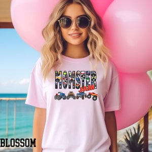 May include: A pink t-shirt with the words "Monster Jam" printed on the front. The words are made up of images of monster trucks.
