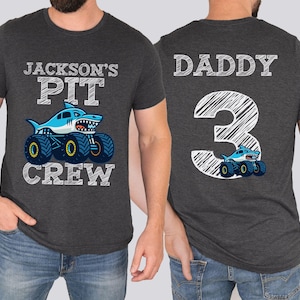 Op de afbeelding: Donkergrijze t-shirts met bijpassende ontwerpen. E&eacute;n shirt heeft een haaien-monstertruck met de tekst "Jackson's Pit Crew". Het andere shirt heeft "Daddy 3" en een haaien-monstertruck.