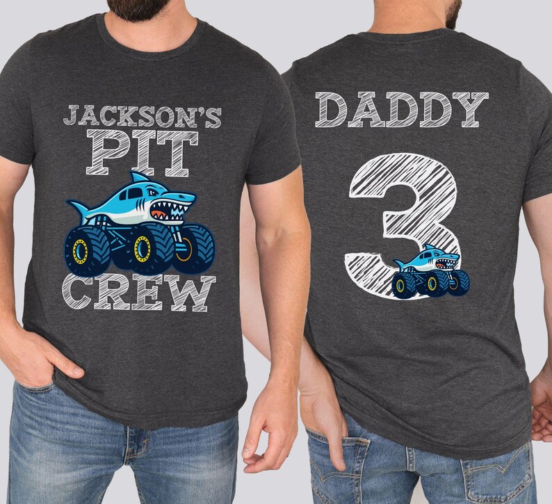 Op de afbeelding: Donkergrijze t-shirts met bijpassende ontwerpen. E&eacute;n shirt heeft een haaien-monstertruck met de tekst "Jackson's Pit Crew". Het andere shirt heeft "Daddy 3" en een haaien-monstertruck.