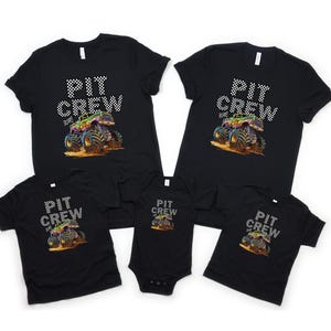 May include: Black t-shirts and a onesie with a colorful monster truck graphic. The text "PIT CREW" is printed above the truck in a checkered pattern. The monster truck is depicted in shades of green, purple, blue, and orange.