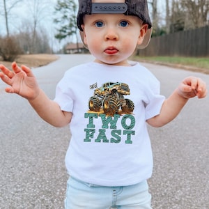 Pictured is a young boy on his second birthday wearing a white t_shirt which says TWO FAST in blue sketch letters along with a large monster truck graphic