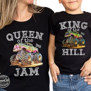 May include: Black t-shirts featuring monster truck designs. One shirt reads "QUEEN of the JAM", the other "KING of the HILL". The trucks are colourful with mud and chequered flags.