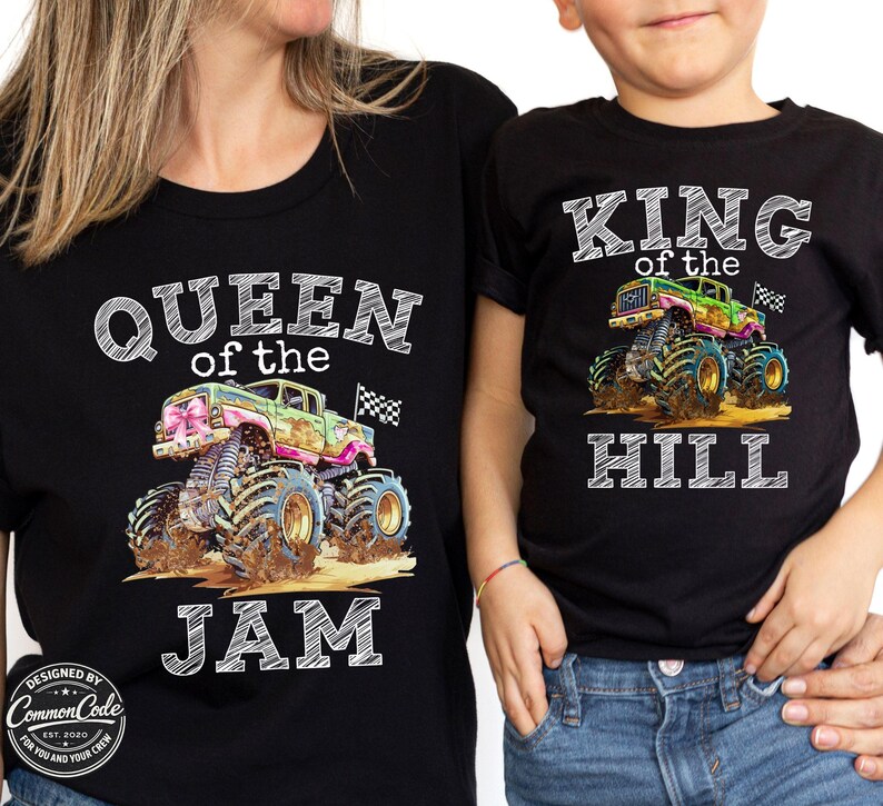 May include: Black t-shirts featuring monster truck designs. One shirt reads "QUEEN of the JAM", the other "KING of the HILL". The trucks are colourful with mud and chequered flags.