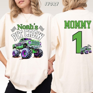 Pictured is a woman wearing a natural colored comfort colors t-shirt with a front back print design which says Noah's Pit Crew with a green and purple monster truck and 2 checkered flags on the front. On the back is custom name MOMMY and a custom number 1 and a small version of the truck