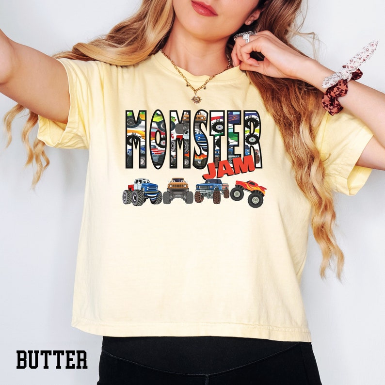 K&ouml;nnte beinhalten: Ein gelbes T-Shirt mit dem Text "Momster Jam" in schwarzen Buchstaben. Die Buchstaben bestehen aus Bildern von Monstertrucks. Am unteren Rand des Shirts befinden sich f&uuml;nf Monstertrucks in einer Reihe.