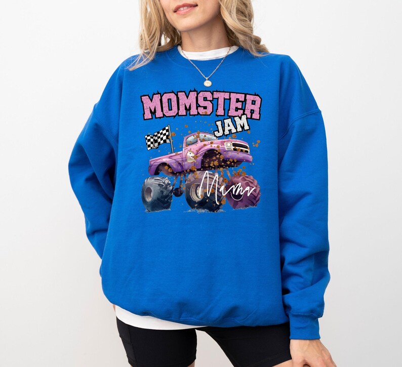 Pu&ograve; includere: Una felpa blu reale con una grafica di un monster truck rosa e il testo "Momster Jam" in rosa. Il camion ha una bandiera a scacchi e la parola "Mom" &egrave; scritta in rosa sul lato.