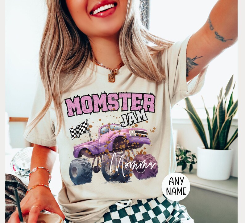 model is wearing a natural tshirt that says "Momster Jam" with a customized name signature "Mama" . Momster is in Pink Varsity Letters in a arch, Jam is in white letters, there is a Pink Monster Truck with a black and white checkered racing flag in the back of the truck. "mama" is in a handwritten text style. Family Matching sizes perfect for all the girls in your group or family. Birthday gift for her, Mother's Day Gift for Her.