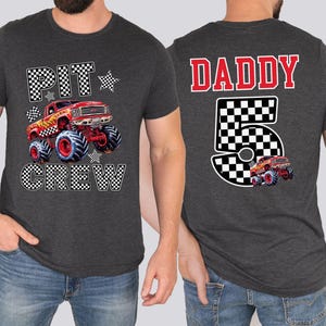 Op de afbeelding: Donkergrijze t-shirts met monster truck graphics. E&eacute;n shirt heeft "PIT CREW" en een rode monstertruck. De andere heeft "DADDY 5" met een monstertruck ontwerp. Beide zijn korte mouwen.