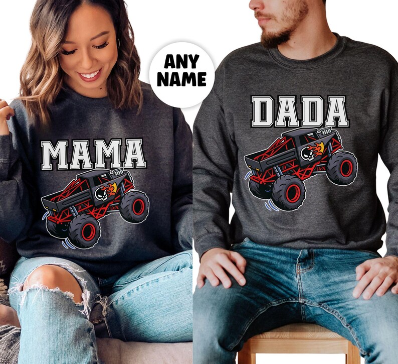 以下が含まれることがあります： 「MAMA」と「DADA」の白いブロック文字がプリントされた、2枚の濃いグレーのスウェットシャツ。それぞれ、黒と赤のモンスターカーのグラフィックが特徴で、スカルと炎が描かれています。スウェットシャツは青いジーンズと合わせて着用されています。