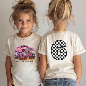 Peut inclure: Deux enfants portant des t-shirts cr&egrave;me. L'un arbore un camion monstre rose avec le texte "A LITTLE DIRT DOESN'T HURT". L'autre pr&eacute;sente un grand chiffre six &agrave; motif damier noir et blanc.