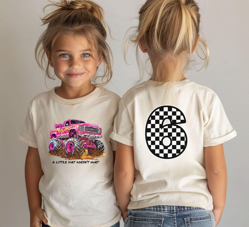 Peut inclure: Deux enfants portant des t-shirts cr&egrave;me. L'un arbore un camion monstre rose avec le texte "A LITTLE DIRT DOESN'T HURT". L'autre pr&eacute;sente un grand chiffre six &agrave; motif damier noir et blanc.