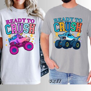 May include: White and grey t-shirts with the text "READY TO CRUSH". One shirt features a unicorn monster truck, the other a shark monster truck. Both designs have colorful graphics and star accents.